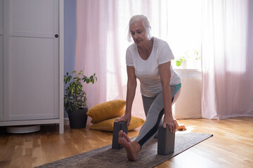Senior aged woman sitting on the yoga mat and stretching her legs