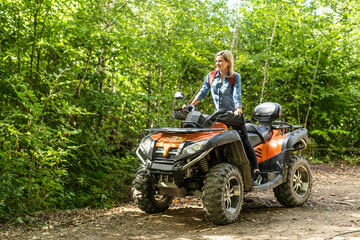 Fototapeta na wymiar Young woman on quad bike on a trail. Young woman driving all terrain vehicle in nature on a sunny day