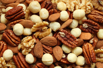 Top view of a pile of large shelled almonds, pecan nuts, walnuts and macadamia nuts arranged randomly. Closeup