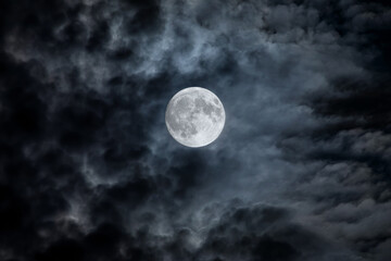 Full moon at night. The illuminated face of the moon is wrapped in a cloud cover that covers it in...