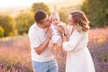 Family portrait mother father and baby on lavender field having fun together. Happy couple with child