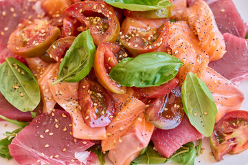 Healthy salad with raw salmon, tuna, green salad, tomato, basil and sesame seeds