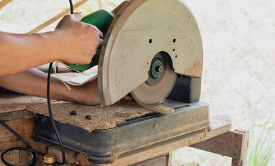 Asian carpenter is using a circular saw to cut wood to construct a storage box on a desk table at his factory. Working as your own boss at home concept