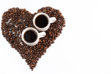 On a white background, a heart made of coffee beans and two cups of espresso. Background with place for writing text. View from above.