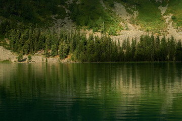 The green slopes of the Altai Mountains are reflected in the water of the Multinskoye Lake of the Katunsky Reserve
