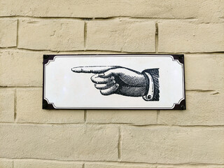 A sign with a hand drawn pointing a direction. Brick wall in the background