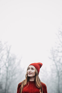 Woman in red hat and sweater walking on foggy mystical morning forest.