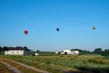 Obraz premium Hot air balloons rise in the sky behind an Amish school in the early morning hours of on a summer day. 