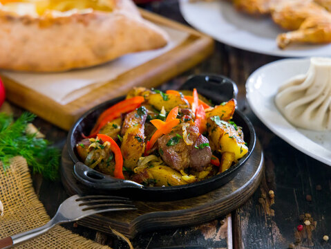 Ojakhuri georgian kitchen with pork, potatoes and vegetables on old wooden table