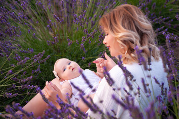 Happy mother with pretty daughter on lavender background. Beautiful woman and cute baby sitting in meadow field. Family holiday in summer day.
