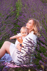Happy mother with pretty daughter on lavender background. Beautiful woman and cute baby playing in meadow field. Family holiday in summer day.