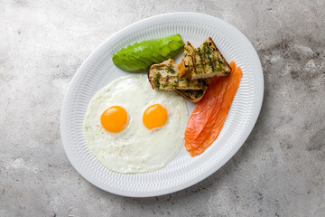 fried eggs with salmon and avocado with fried croutons on white plate top view