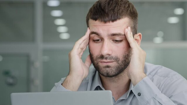 Close-up tired pensive businessman looking at laptop screen suffering from overwork feeling headache painful symptom migraine rubbing temples young sad man sitting in office feels unwell from workload