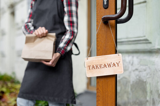 woman holds a wooden sign with the inscription takeaway, open or closed at the door of a restaurant or coffee shop. the working hours of the restaurant or the food and beverage delivery service. to