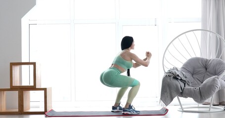 Fototapeta premium Young woman training with elastic resistance rubber band, beautiful female doing exercises alone at home, workout indoors