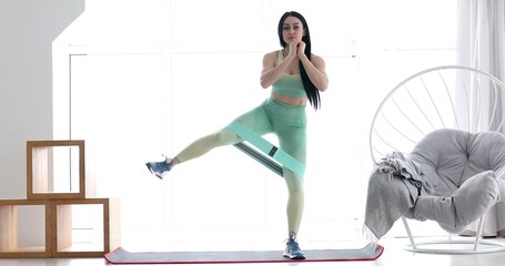 Young sportswoman doing exercises with rubber band on a mat at home.