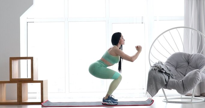 Woman does exercises for legs, build up the muscles of the legs and buttocks, wearing sportive outfit, at home.