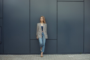 Full length photo of thinking young businesswoman standing on one leg leaning on gray wall of...