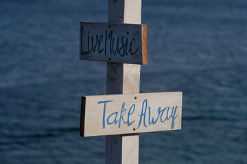 View of wooden signs for Take away and Live music and the sea in the background on the beach of...