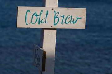 View of wooden signs for Cold Brew and the sea in the background on the beach of Mylopotas in Ios Greece
