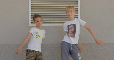 Portrait of cute smiling preteen boys posing together, make dance movements with the body, grey frame backdrop, summer lifestyle. Happy schoolchildren celebrating start of school year. 