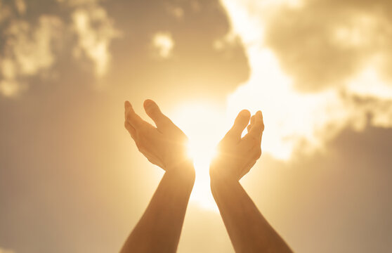 worshiping hands up to the bright golden sunlight 
