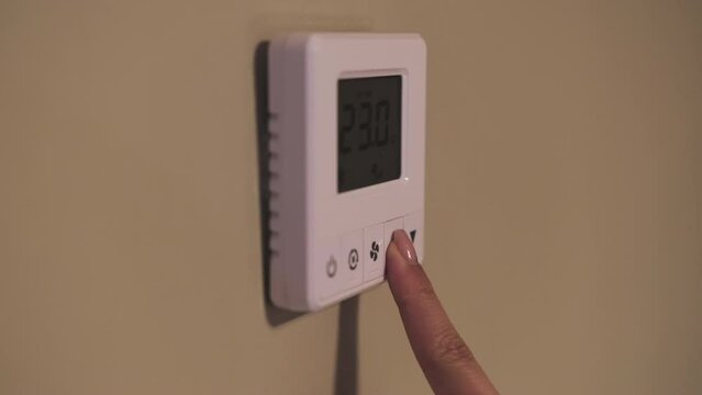 Female person finger switches on temperature controller of air conditioner. Adult woman chooses comfortable temperature of device closeup
