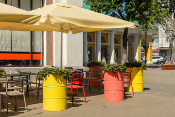 Fototapeta na wymiar Street cafe - tables, chairs, umbrellas, colorful flower beds-barrels with flowers, summer day
