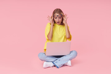 Full leight Portrait of a young surprised girl in casual clothes with a laptop in her hands on a pink background. The concept of learning and job search online