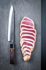 Traditional Japanese tuna tataki filets slices with Japanese Yanagiba knife served as top view on a design stone board