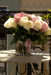 Blooming beautiful pink Petunia flowers and white watering can stands on table. Metal forged furniture on balcony on sunny summer day. Flowers on balcony