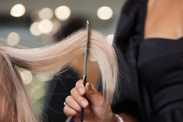 Hair stylist makes bouffant using comb on thin strands. Shatush technique for hair lightening.