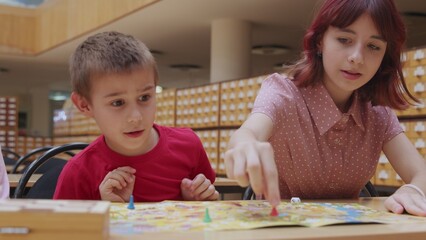 4K. Children play a board game in the library, sitting at the table.