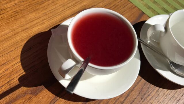 hot cranberry and currant tea two teapots stand on a wooden table from them poured into a white cup steaming drink. High quality 4k footage