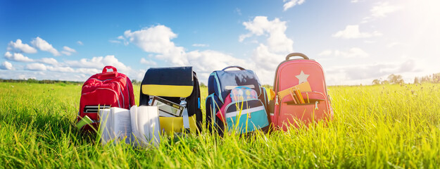 Children's schoolbags of different colours standing on the green field