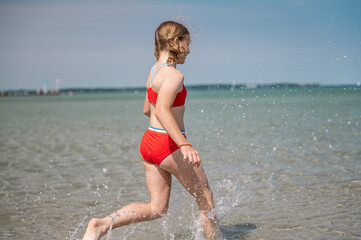 Fototapeta na wymiar Happy teen girl running and splashing water in turquoise sea at summer holidays
