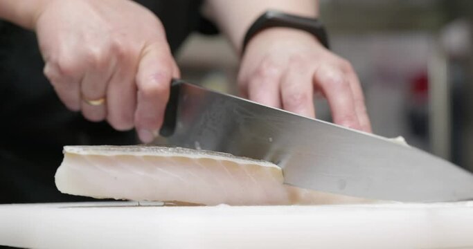 cutting cod cod fillet on a plastic board in professional restaurant kitchen. Close up arm with a knife 