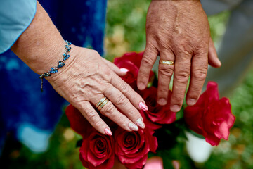 hands of old people with wedding rings over flowers in shallow depth of field