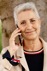 natural portrait of an older woman with gray hair, with a serene and happy gesture looking at the camera using her mobile phone.