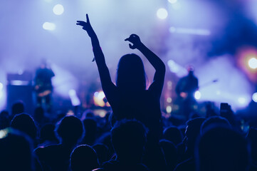 Silhouette of a woman with raised hands on a concert - obrazy, fototapety, plakaty