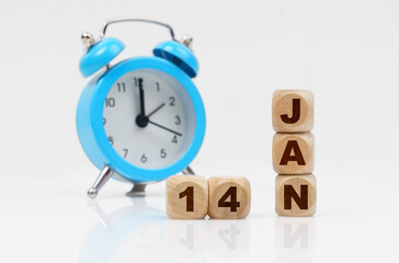 Wooden cube calendar for January 14, next to a blue alarm clock.