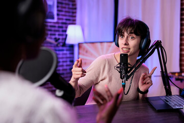 Female presenter interviewing young woman with podcast equipment, having conversation to broadcast...