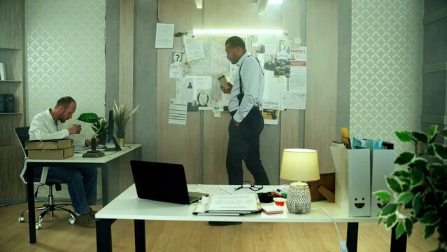Concentrated detective going back and forth with coffee while reflecting on homicide investigation. Handsome policeman thinking about case while his partner working on computer High quality 4k footage