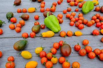 Ripe tomatoes and green peppers are scattered on a wooden table, upper view. Background from fresh tomatoes and pepper for publication, poster, screensaver, wallpaper, postcard, banner, cover, post