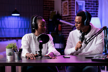 POV of man and woman recording live discussion on camera, doing podcast episode together. Lifestyle influencer talking to female guest in studio with rpg neon lights and equipment.