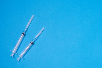 Two plastic disposable syringes lie on a blue background on the left, vaccination, preparation for an injection, health care, immunization of the population