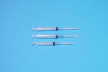 Three plastic disposable syringes lie on a blue background in the center of the composition, vaccination, preparation for injection, healthcare, immunization of the population