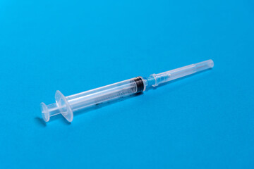 On a blue background lies a disposable plastic closed syringe, preparing for an injection, medical care