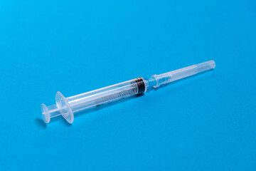 Fototapeta premium On a blue background lies a disposable plastic closed syringe, preparing for an injection, medical care
