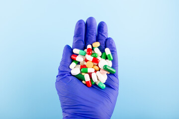 Hand in a blue medical glove with a handful of tablets and pills. Medicine concept.